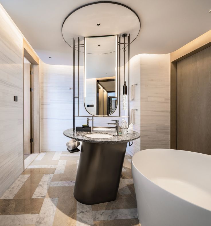 Modern luxury bathroom with a unique sculptural circular vanity, asymmetrical pedestal base, integrated mirror, and round ceiling light feature.