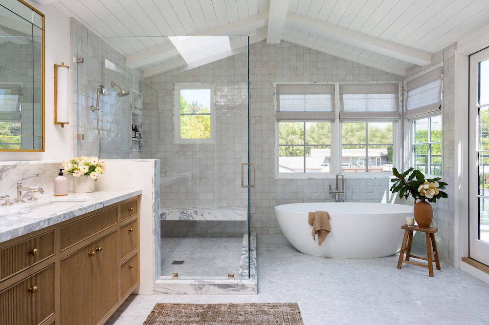 A bright and spacious modern bathroom with a white vaulted ceiling, featuring a frameless glass walk-in shower as its core, alongside a freestanding tub and a wooden vanity.